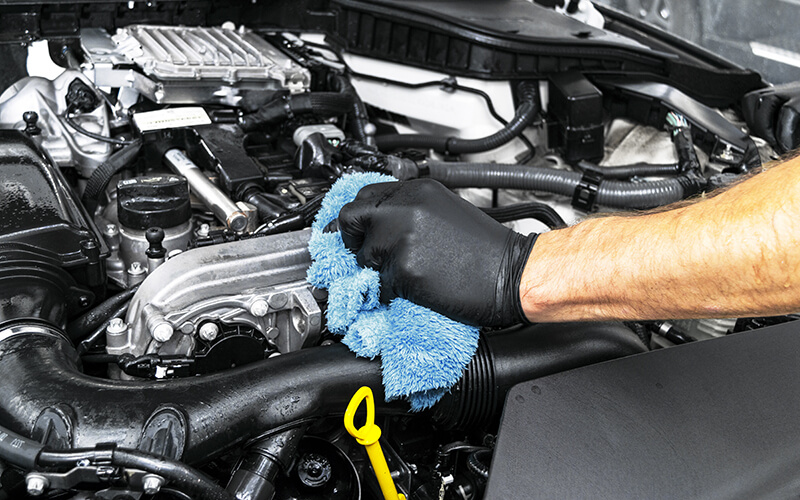 Person cleaning the engine compartment of a vehicle